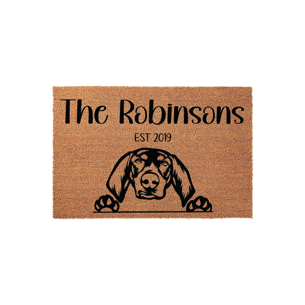 Personalized dog breed coir doormat featuring a custom family name and established year, showcasing a detailed black graphic of a hound dog peeking over the bottom edge against a natural brown textured fiber background for a
