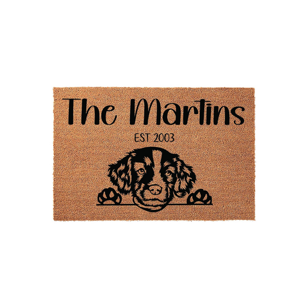 Personalized Spaniel Dog Doormat featuring a cute illustrated dog peeking over the bottom edge, with custom family name text and established year printed in black on a natural brown coir fiber background for a welcoming home