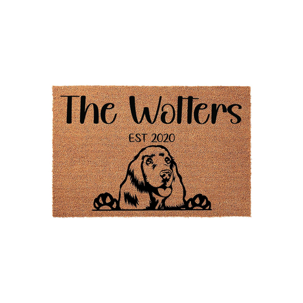 Personalized Cocker Spaniel family doormat featuring a cute dog illustration peeking over the bottom edge, printed on a natural tan coir mat with custom family name text and established year for a welcoming home entrance decor.