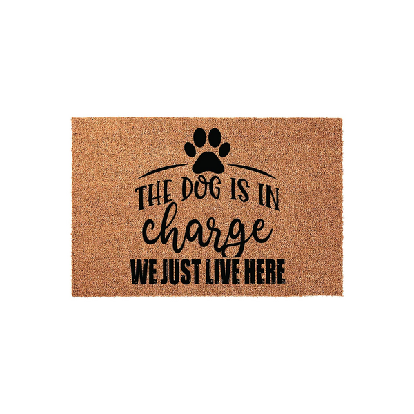 Funny Dog Lover Coir Doormat featuring a black paw print icon and the humorous text The Dog Is In Charge We Just Live Here printed in a mix of bold block and script fonts on a natural brown textured coconut fiber welcome mat