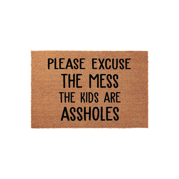 Funny coir doormat featuring the text Please Excuse The Mess The Kids Are Assholes in bold black lettering, set against a natural brown coconut fiber background for a humorous and welcoming entryway decor piece for any busy