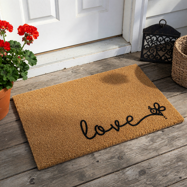 Love Bee Coir Doormat featuring a natural tan fiber texture with the word love written in black cursive script, where the letter e is creatively stylized as a cute bumblebee, set against a clean white studio background for a