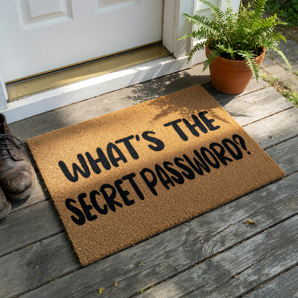 Funny What's The Secret Password doormat featuring bold black text printed on a natural tan coir fiber mat, providing a humorous and welcoming touch to your front porch entryway decor for guests arriving at your home.