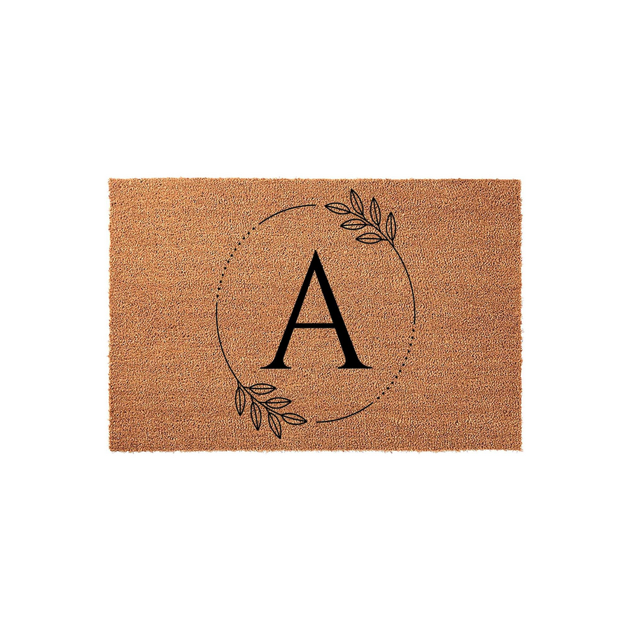 Personalized monogram coir doormat featuring a large black letter A centered inside a delicate circular frame of thin dotted lines and minimalist botanical leaf illustrations, set against a natural brown textured coconut fiber