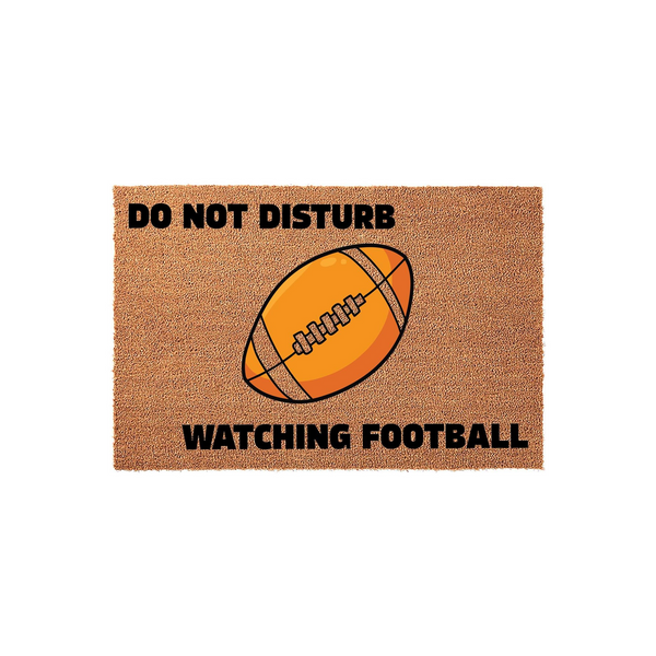 Football Do Not Disturb Doormat featuring a brown coir texture with a large illustrated orange football in the center and bold black text that reads Do Not Disturb Watching Football for a fun sports themed home entrance decor