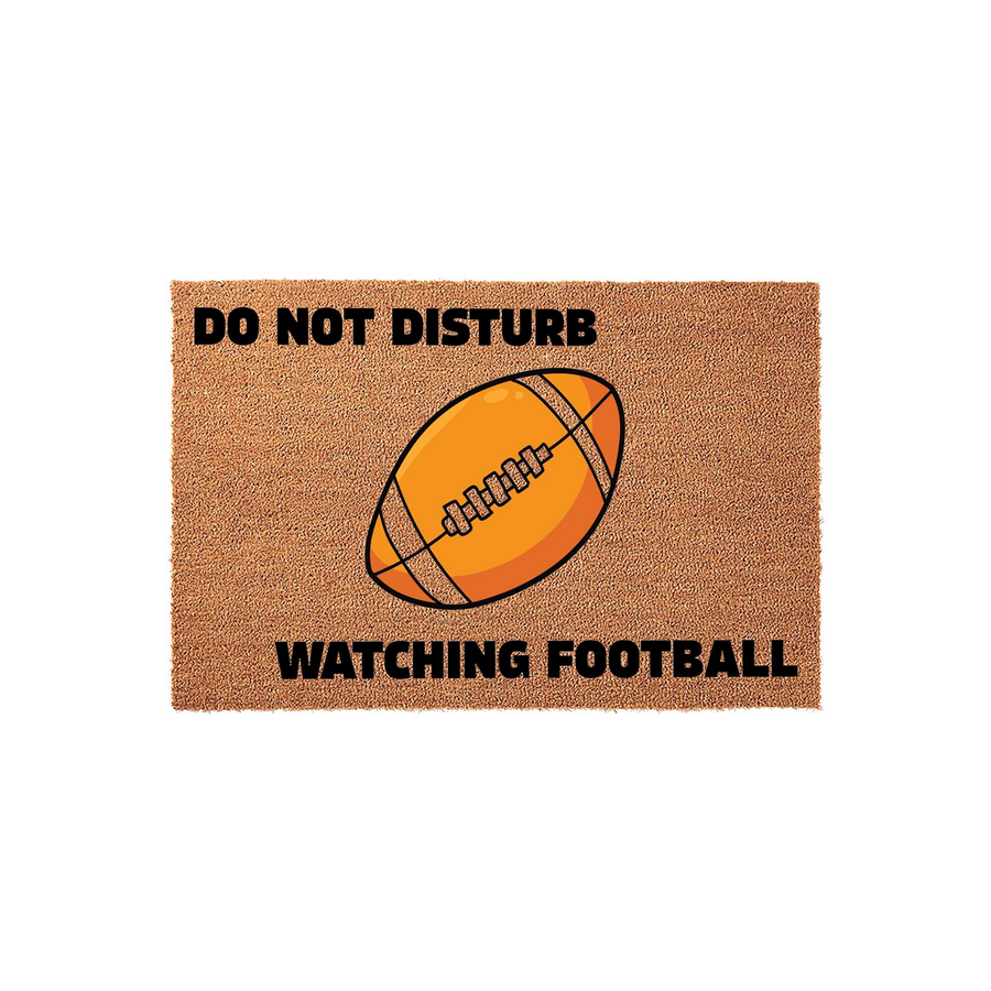 Football Do Not Disturb Doormat featuring a brown coir texture with a large illustrated orange football in the center and bold black text that reads Do Not Disturb Watching Football for a fun sports themed home entrance decor