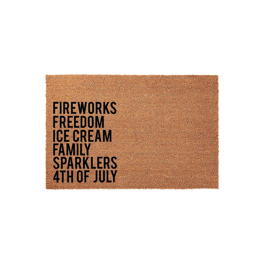 Fourth of July coir doormat featuring a natural tan fiber texture and bold black text that lists festive holiday words like fireworks, freedom, ice cream, family, and sparklers for a patriotic outdoor entryway decor style.