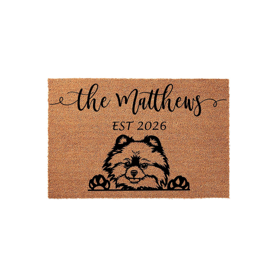 Personalized Pomeranian doormat featuring a cute dog illustration peeking over the bottom edge, printed on natural coir fiber with custom family name text and an established year on a clean white background for a welcoming home