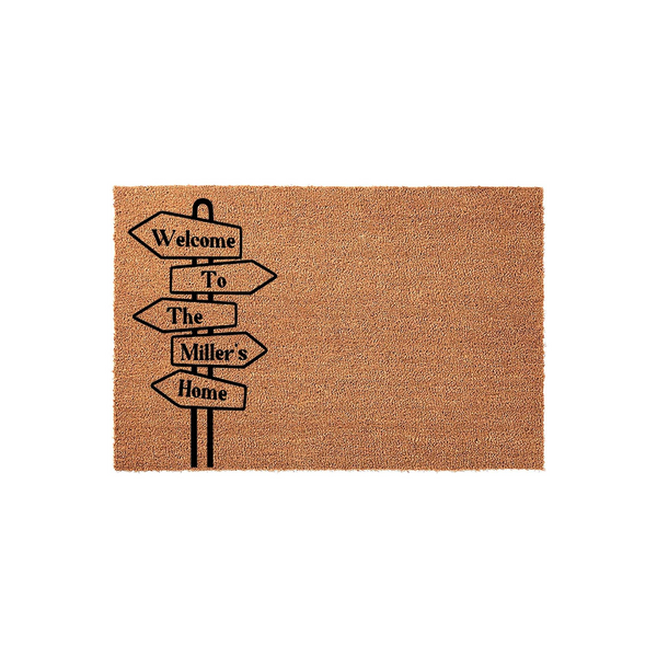 Personalized Welcome To The Home Coir Doormat featuring a black directional signpost graphic on a natural brown fiber background, providing a welcoming entrance for any family home with a custom last name space on the