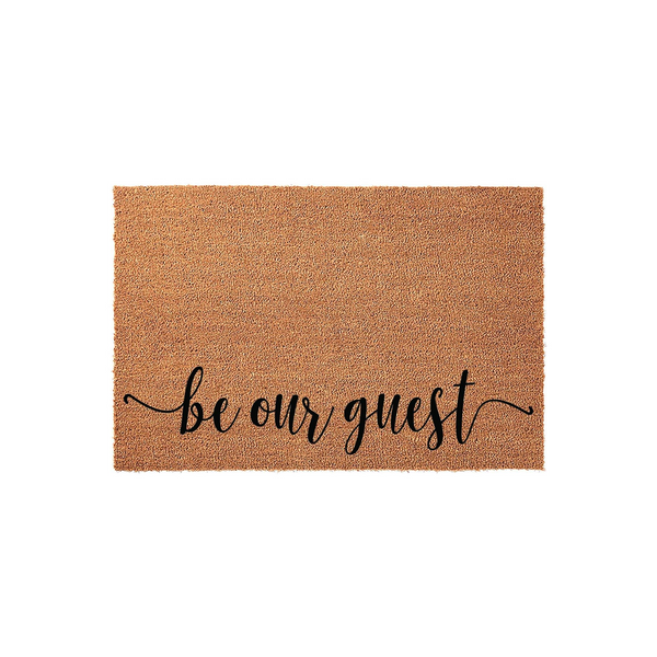 Be Our Guest coir doormat featuring a natural tan fiber texture and elegant black script lettering centered on the front, providing a welcoming and functional entryway decor piece for your home porch or front door area.