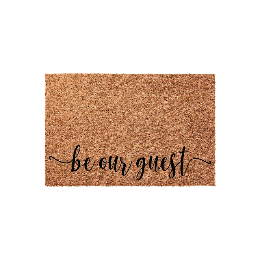 Be Our Guest coir doormat featuring a natural tan fiber texture and elegant black script lettering centered on the front, providing a welcoming and functional entryway decor piece for your home porch or front door area.