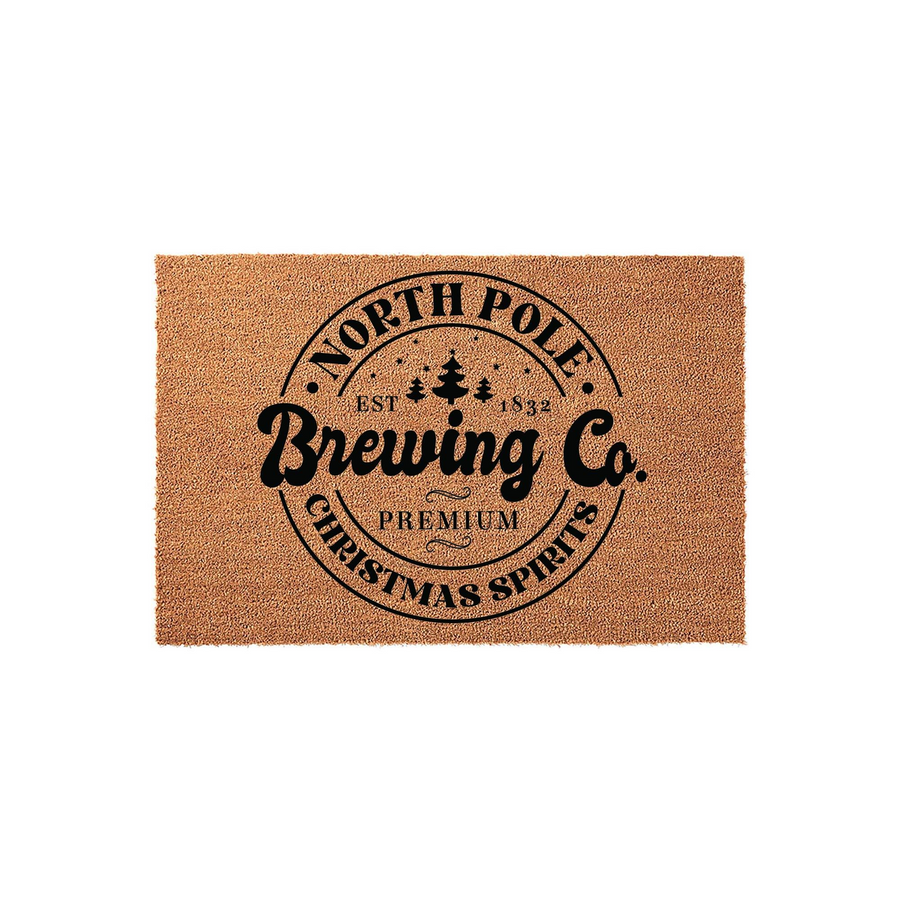 North Pole Brewing Co. Christmas doormat featuring a natural coir texture with a black circular logo design that includes pine trees and festive holiday text, creating a fun seasonal welcome for your front porch entryway decor.