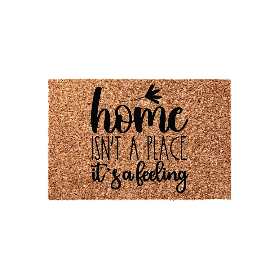 Home Isn't A Place It's A Feeling coir doormat featuring a natural brown fiber texture and bold black typography, centered on a plain white background to showcase the welcoming front porch decor style for your entryway or