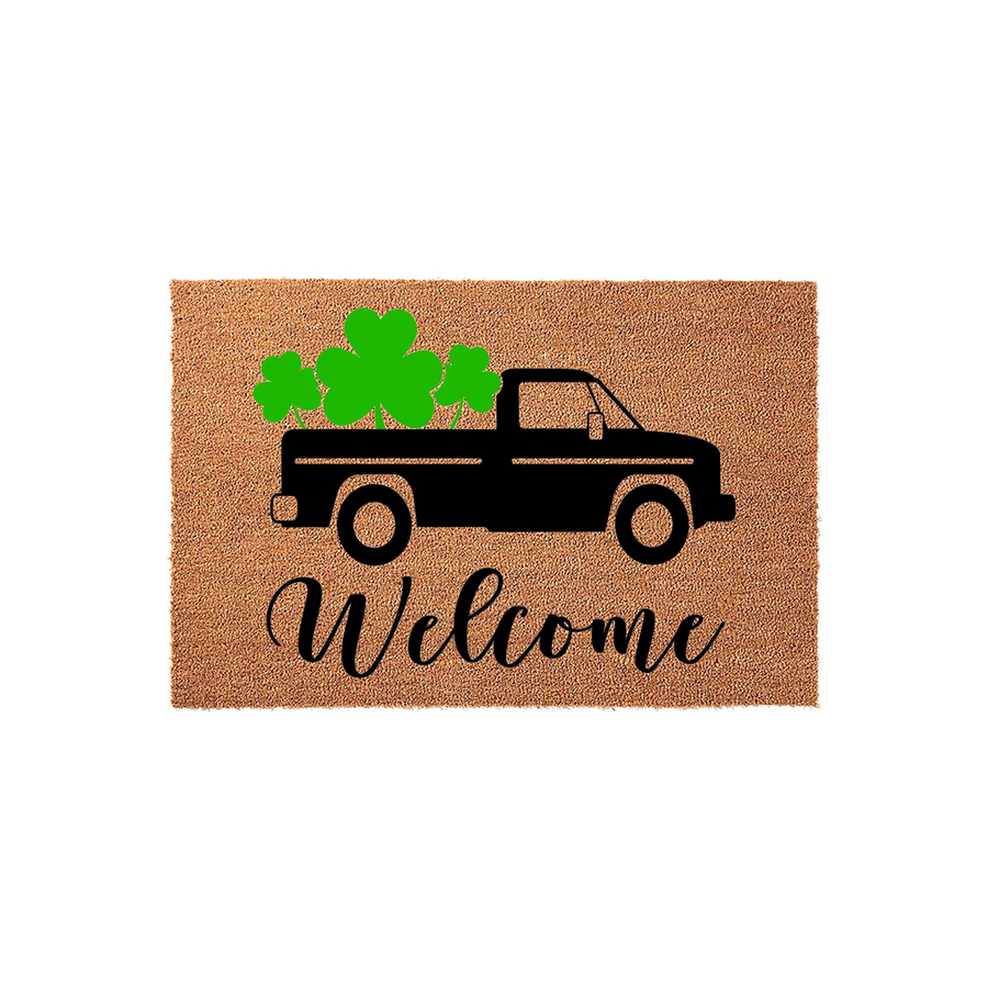St. Patrick's Day welcome doormat featuring a black truck silhouette carrying bright green shamrocks on a natural coir background, with the word Welcome written in elegant black script lettering below the truck design.
