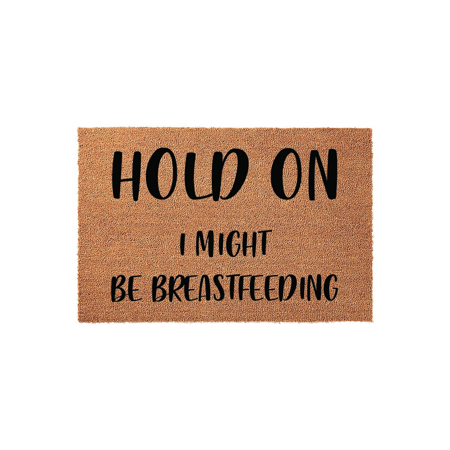 Funny Breastfeeding Welcome Doormat featuring a natural coir texture with bold black lettering that reads Hold On I Might Be Breastfeeding, making it a humorous and relatable home decor piece for any new mom or nursing parent's