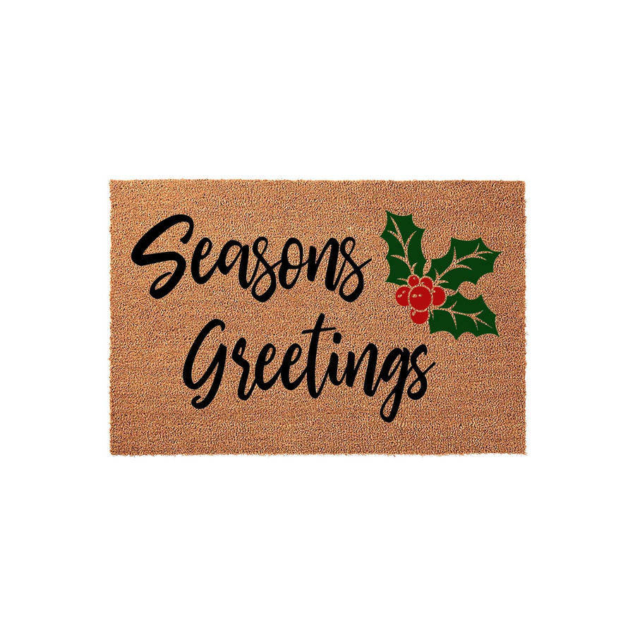 Seasons Greetings Christmas coir doormat featuring a natural tan fiber texture with black cursive lettering and a festive illustration of green holly leaves and bright red berries on a plain white studio background for holiday