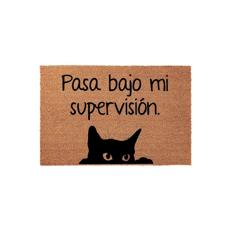 Funny cat doormat featuring a black silhouette of a cat peeking over the bottom edge, with the Spanish text Pasa bajo mi supervision printed in black lettering on a natural brown coir fiber background for a whimsical entryway