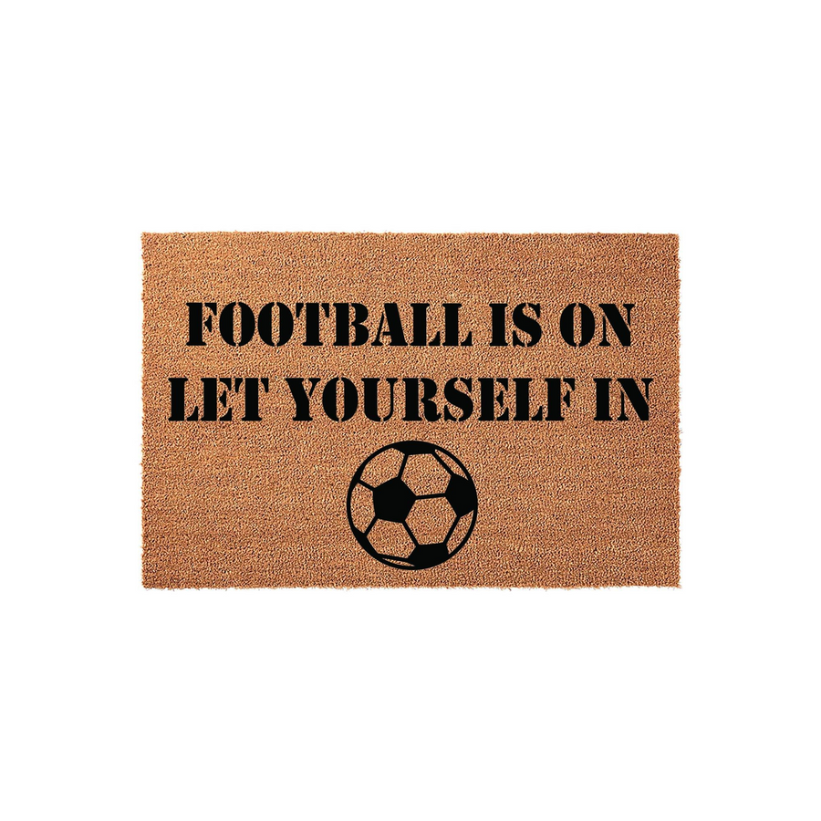 Football Is On Let Yourself In coir doormat featuring a natural brown fiber texture and bold black stencil text, accented with a classic soccer ball graphic centered at the bottom for a fun sports-themed entryway decor piece.