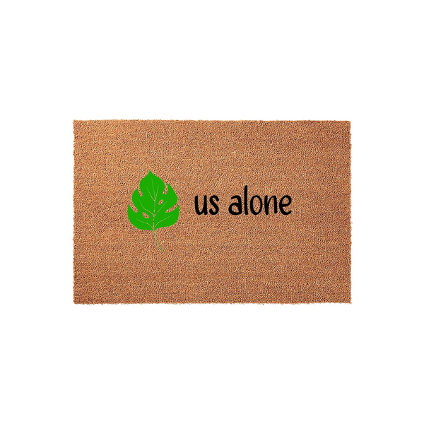 Monstera Leaf Welcome Doormat featuring a natural coir texture with a bright green tropical leaf illustration and the text us alone printed in a simple black font, centered on a clean white studio background for a modern entryway.