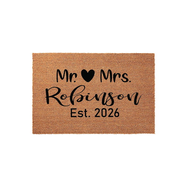 Personalized Mr. and Mrs. coir doormat featuring a black heart icon, a custom family name in elegant script, and the established year 2026, all printed on a natural brown textured fiber mat against a clean white studio background.