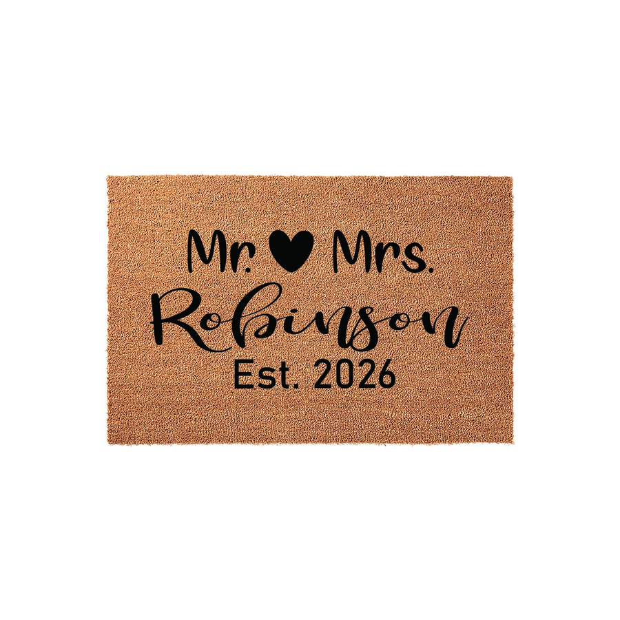 Personalized Mr. and Mrs. coir doormat featuring a black heart icon, a custom family name in elegant script, and the established year 2026, all printed on a natural brown textured fiber mat against a clean white studio background.