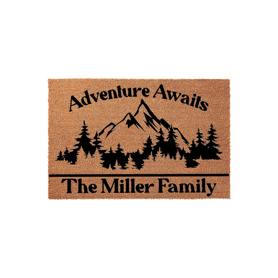 Personalized Adventure Awaits mountain doormat featuring a black graphic of a forest and mountain range on a natural coir background, with space at the bottom to customize with a family name for a rustic outdoor home entrance