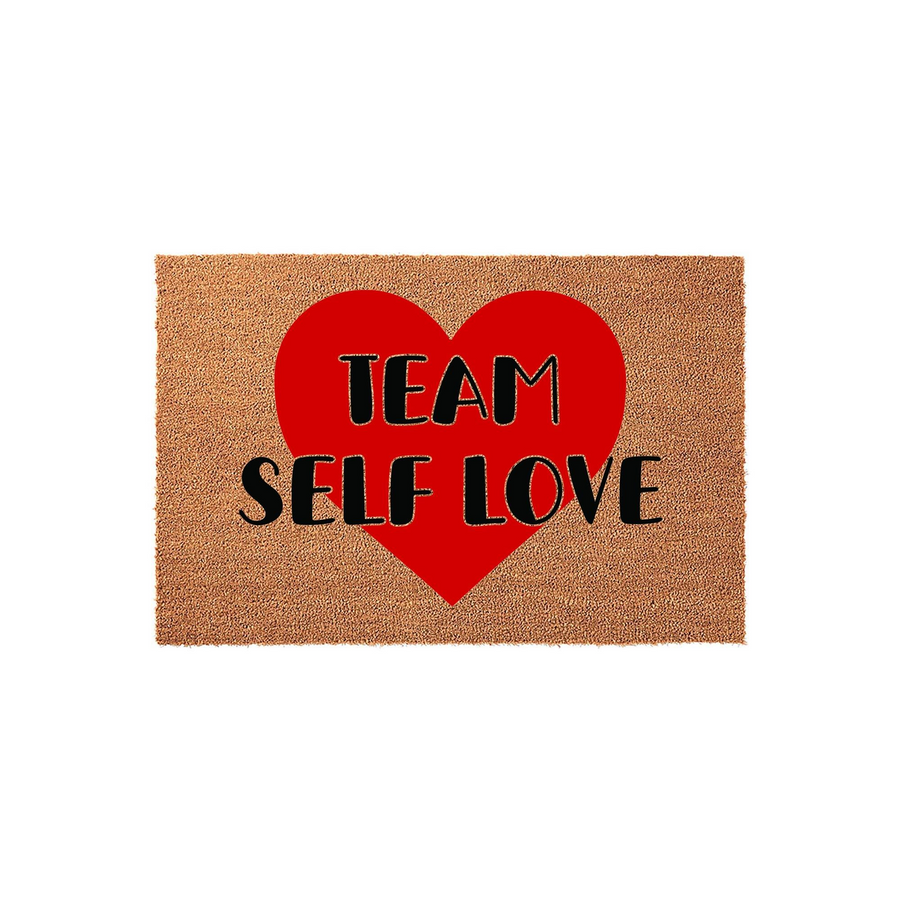 Team Self Love coir doormat featuring a large, bold red heart graphic centered on a natural brown textured fiber background, providing a welcoming and motivational entryway accent for your home decor with its clear black printed