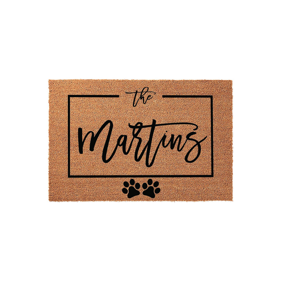 Personalized family name coir doormat featuring a rectangular black border, elegant script text, and two cute paw prints at the bottom, making it a charming and durable welcome mat for any pet-loving household entrance.
