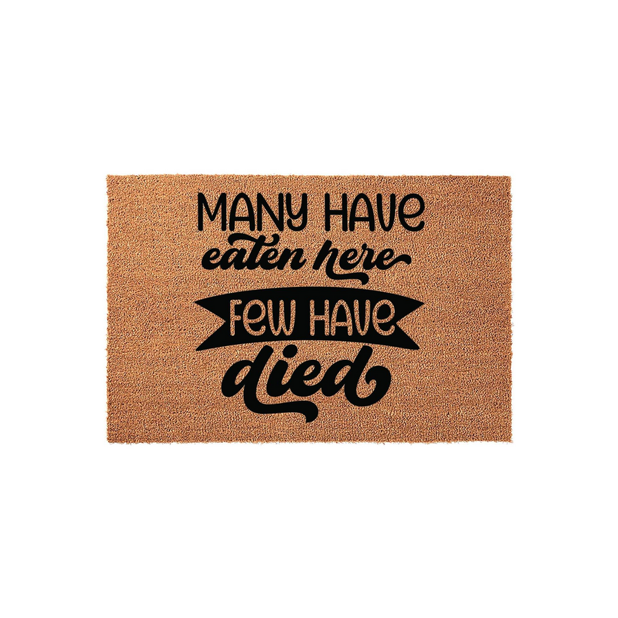 Funny Kitchen Doormat with the text Many Have Eaten Here Few Have Died printed in bold black lettering on a natural tan coir fiber mat, creating a humorous and welcoming accent for your home entryway or kitchen floor decor.
