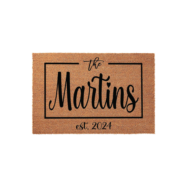 Personalized family name coir doormat featuring a rectangular border design with the text the Martins and the established year 2024 printed in black ink on a natural brown coconut fiber mat against a clean white studio background.
