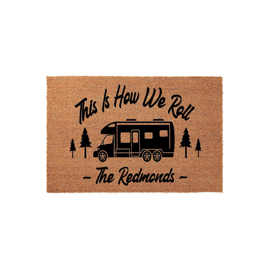Personalized Camping Doormat featuring a black motorhome graphic, pine trees, and the text This Is How We Roll with a customizable family name, all printed on a natural tan coir fiber mat against a clean white studio background.