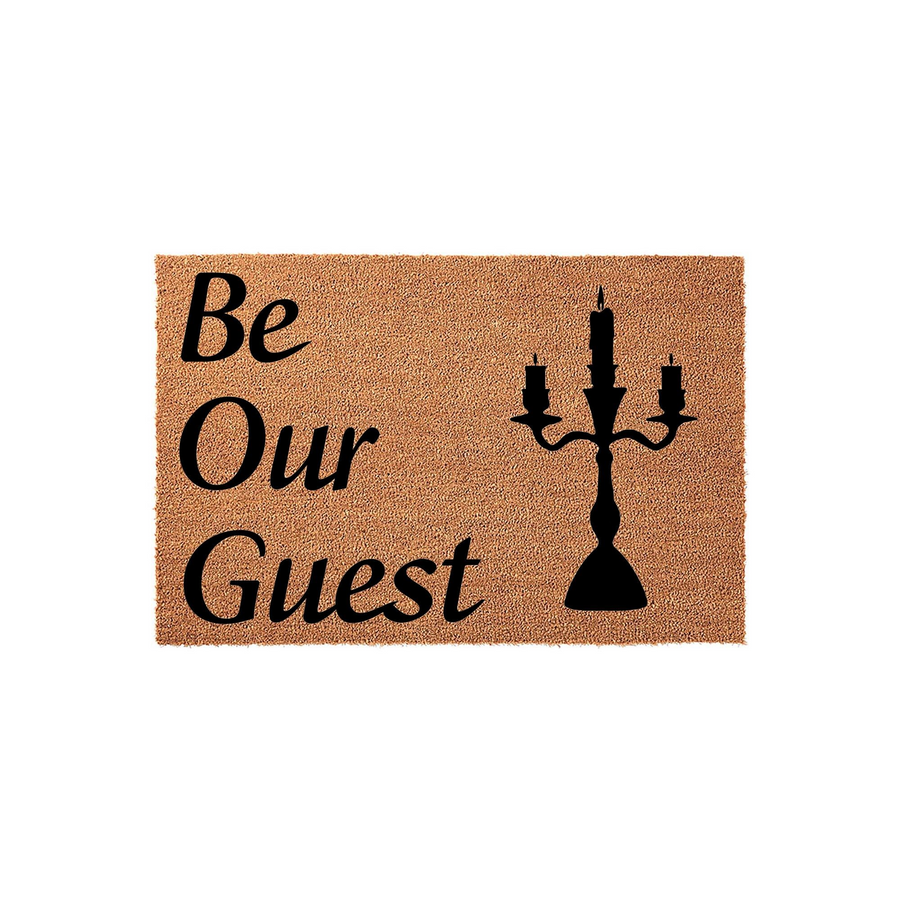Be Our Guest coir doormat featuring a black silhouette of a classic three-candle candelabra printed on the right side, set against a natural tan textured fiber background for a welcoming entryway decor piece.