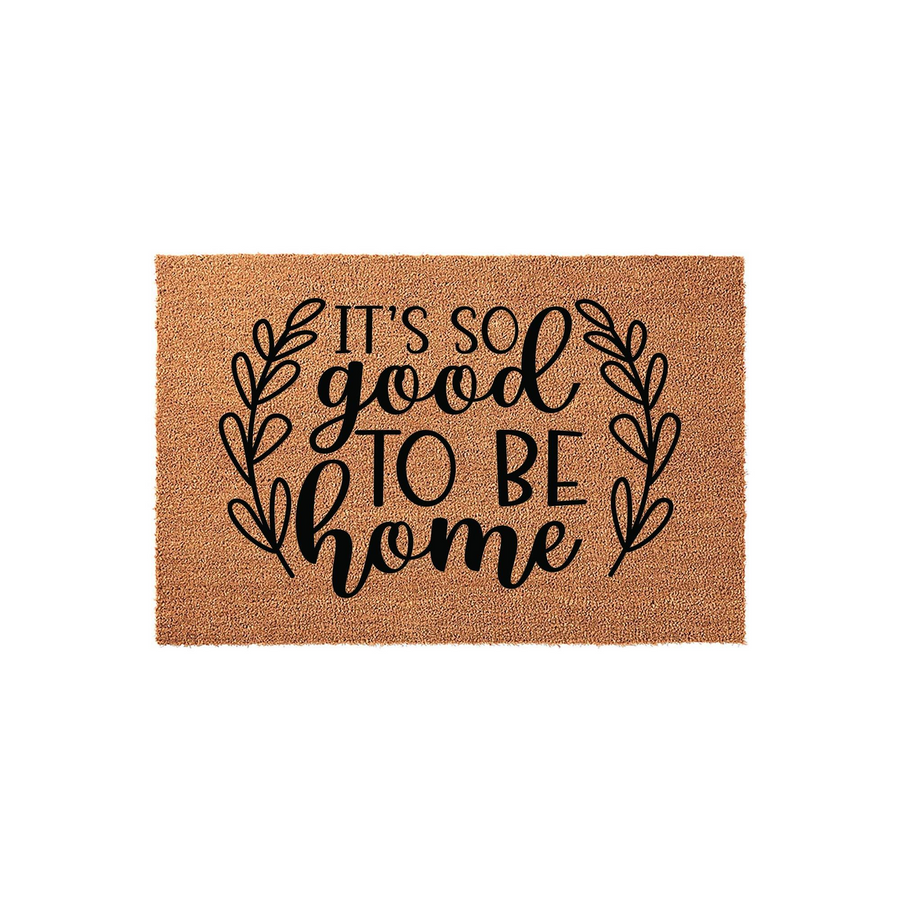 It's So Good To Be Home coir doormat featuring a natural brown fiber texture and black printed text surrounded by a decorative leaf wreath design, creating a welcoming entrance piece for your front porch or entryway floor decor.