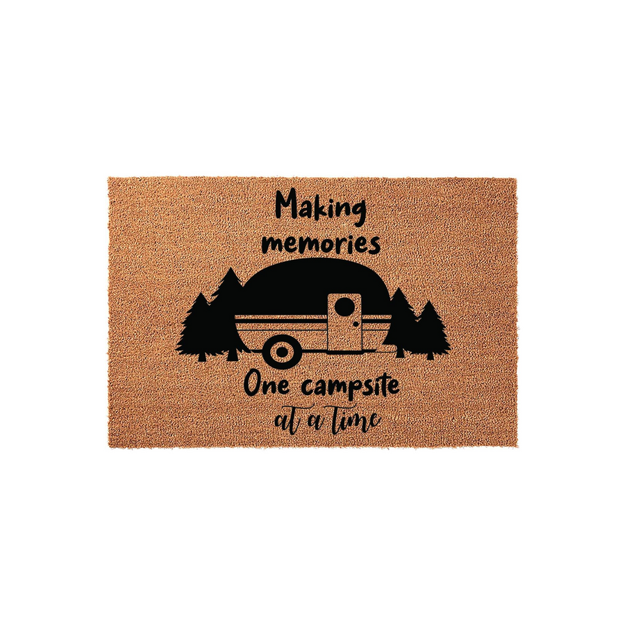 Camping themed coir doormat featuring a black graphic of a vintage camper trailer nestled among pine trees, with the text Making memories one campsite at a time printed in a playful font on a natural tan textured background.