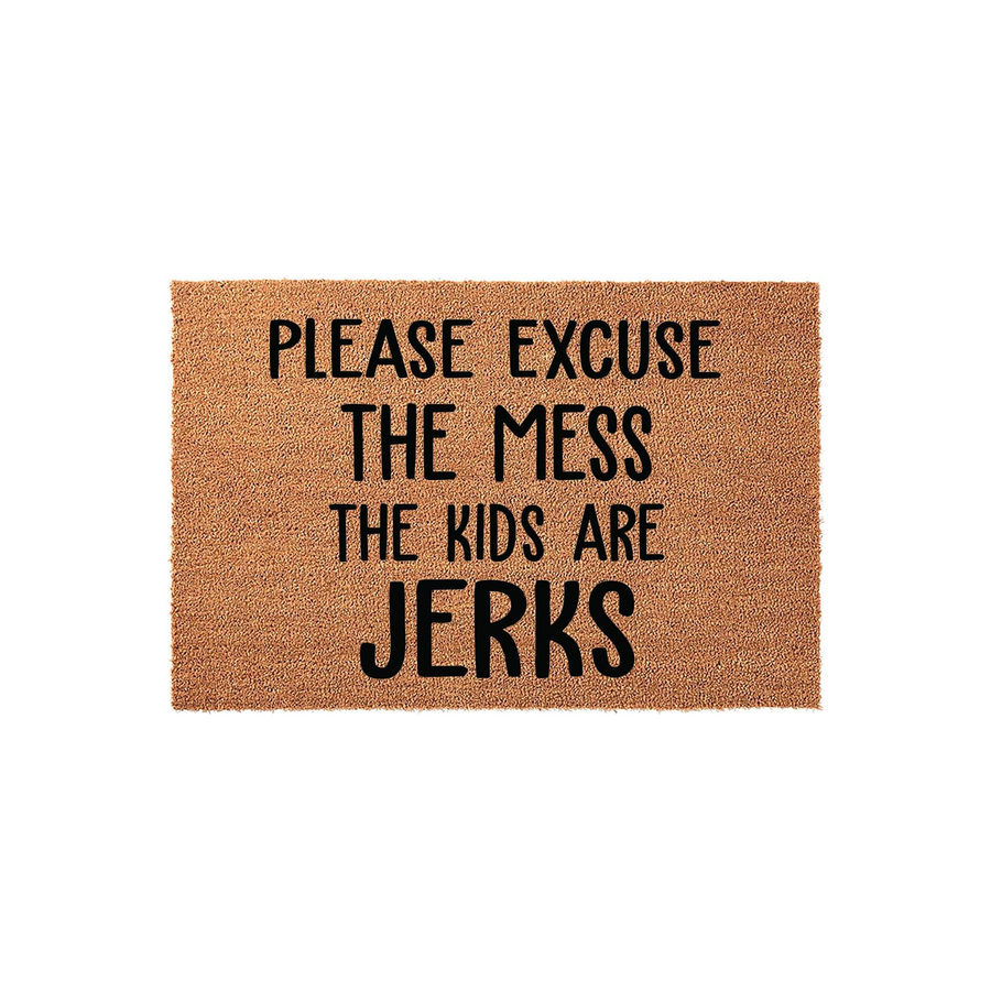 Funny Welcome Doormat featuring the text Please Excuse The Mess The Kids Are Jerks printed in bold black lettering on a natural brown coir fiber mat, creating a humorous and relatable entryway decor piece for any busy family home.