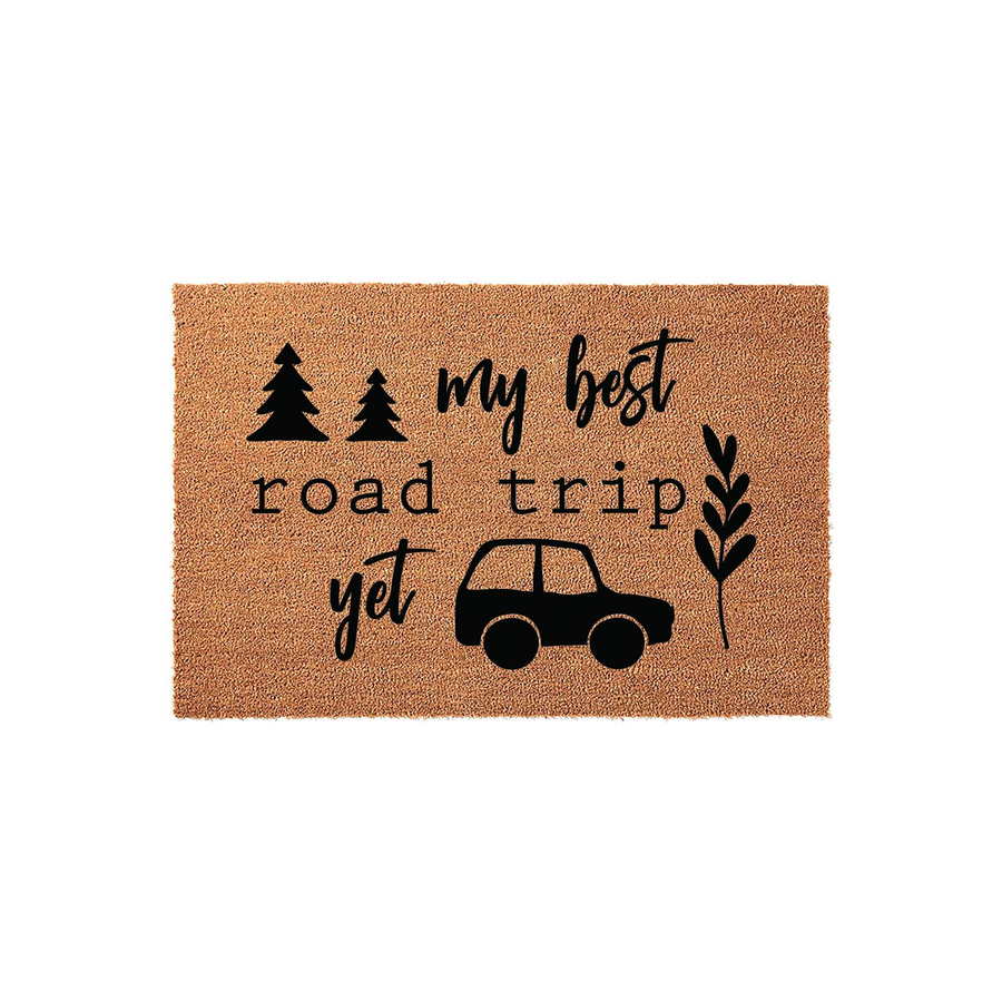 My Best Road Trip Yet coir doormat featuring a natural tan fiber texture with black printed graphics of a small car, pine trees, and a leafy branch, creating a charming outdoor welcome mat for any travel enthusiast's front porch