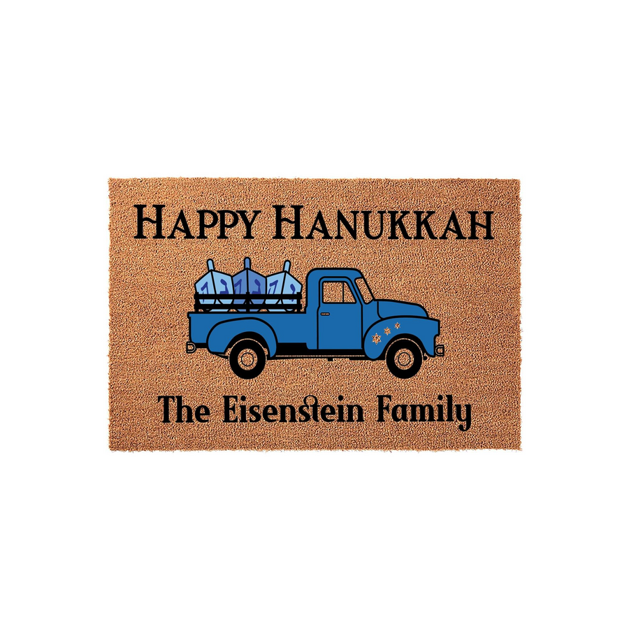 Personalized Hanukkah doormat featuring a blue vintage truck carrying a menorah, with the text Happy Hanukkah and a space for a family name printed on a natural coir fiber background for a festive holiday entryway decoration.