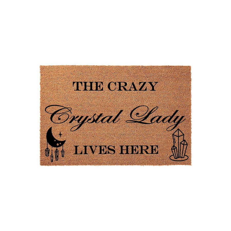 Crazy Crystal Lady coir doormat featuring a natural brown fiber texture with black printed text that reads The Crazy Crystal Lady Lives Here, accented by a crescent moon and crystal cluster illustrations on a plain white