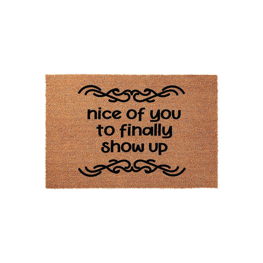 Funny Welcome Doormat featuring the text nice of you to finally show up in bold black lettering, centered on a natural brown coir fiber mat with decorative scrollwork accents above and below the humorous greeting for your front