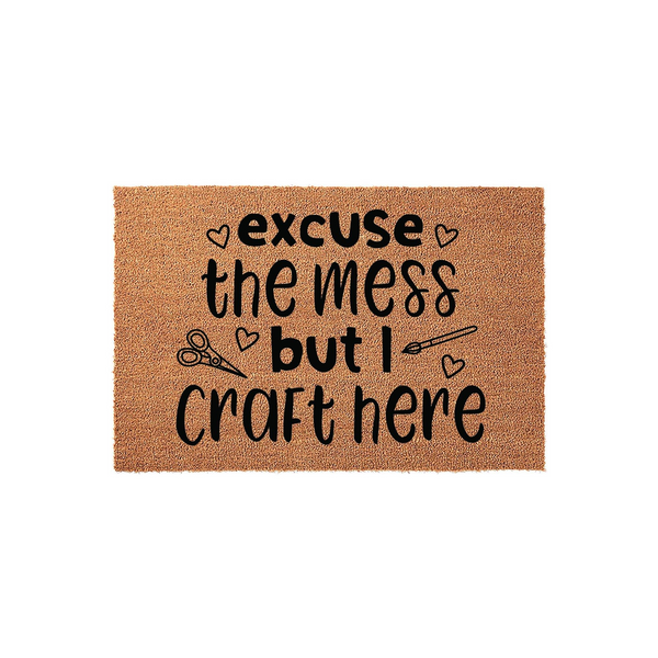 Excuse the mess but I craft here coir doormat featuring black text and cute icons of scissors and a paintbrush, set against a plain white background to highlight the natural fiber texture of this fun entryway floor mat for