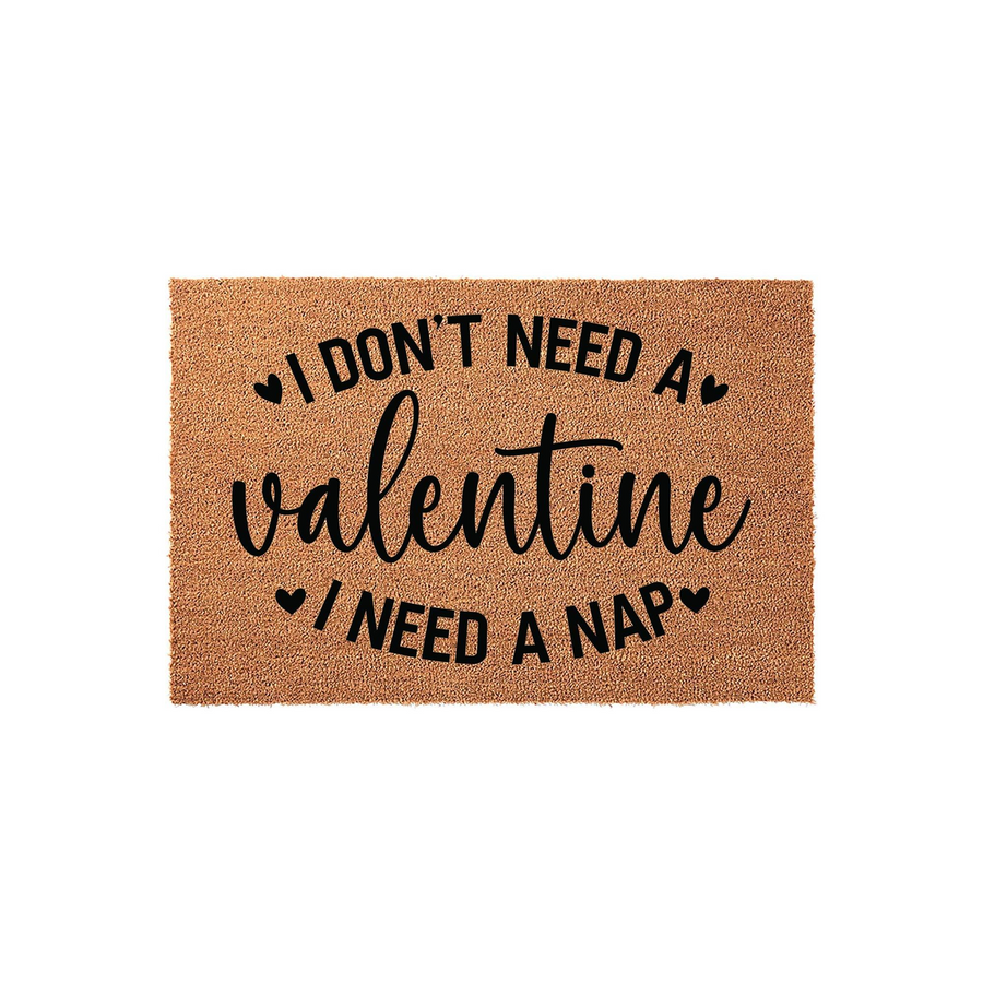 Funny Valentine's Day doormat made of natural coir fiber, featuring the black printed text I Don't Need A Valentine I Need A Nap with small heart accents, displayed against a clean white studio background for a festive home