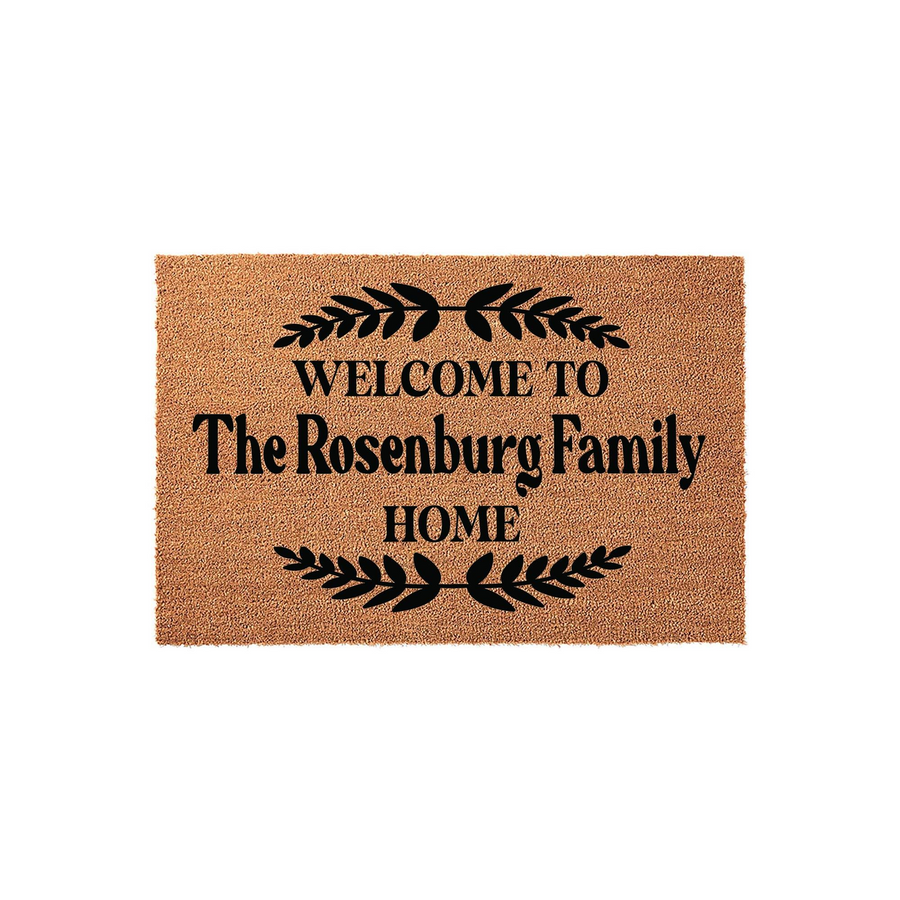 Personalized Family Name Coir Doormat featuring a natural tan fiber texture with black text that reads Welcome to the family home, accented by decorative leaf branches above and below the custom text on a clean white background.