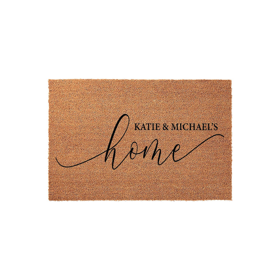Personalized coir doormat featuring a natural tan fiber texture and elegant black script lettering that reads home, customized with a couple's names to create a welcoming entrance for any new house or apartment front door.