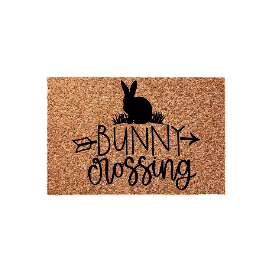 Bunny Crossing coir doormat featuring a black silhouette of a rabbit sitting in grass above the text, designed with a rustic arrow graphic on a natural tan fiber background for a charming spring or Easter front porch entryway