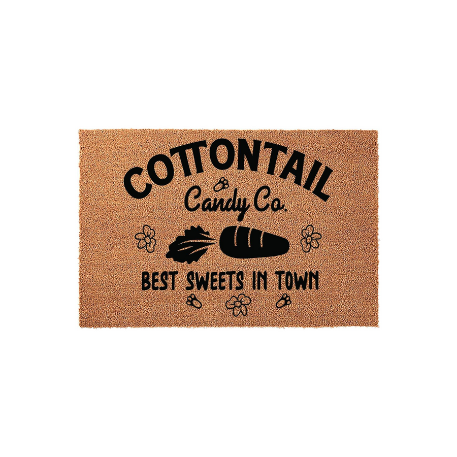 Cottontail Candy Co. natural coir doormat featuring a whimsical black printed design of a carrot, a candy bar, and small flowers, with the text Best Sweets In Town displayed on a textured brown fiber surface for a fun entryway