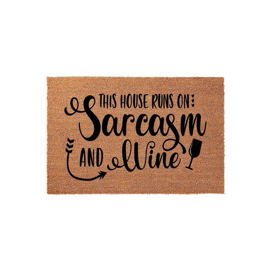 Funny Sarcasm and Wine Coir Doormat featuring a natural tan fiber texture with bold black text that reads This House Runs On Sarcasm and Wine, complete with a decorative arrow and a wine glass icon for a humorous front porch