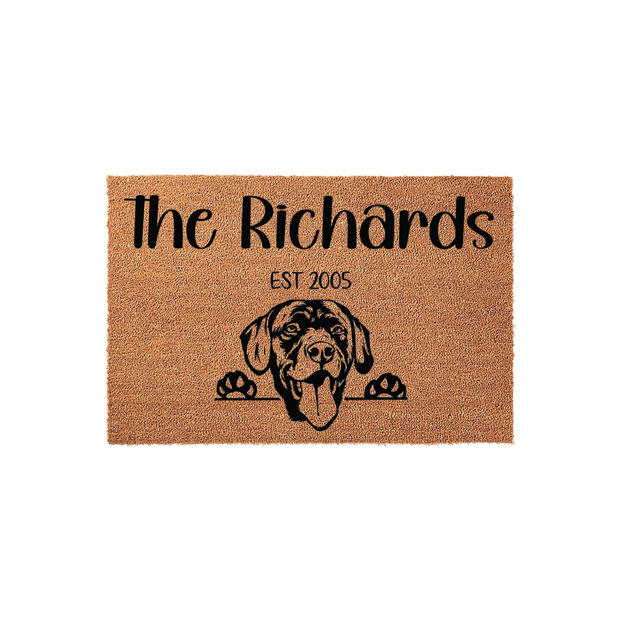 Personalized Labrador Retriever doormat featuring a natural coir texture with a black printed illustration of a happy dog peeking over the edge, customized with a family name and established year on a clean white studio