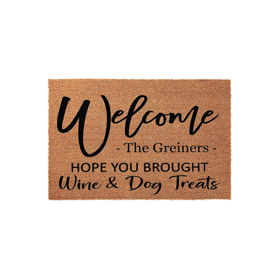 Personalized coir doormat featuring the text Welcome The Greiners Hope You Brought Wine and Dog Treats in a mix of elegant script and bold block lettering, set against a natural brown textured fiber background for a fun home