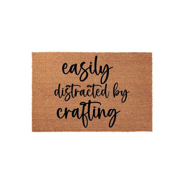 Easily Distracted by Crafting coir doormat featuring a natural brown fiber texture and bold black script lettering, perfect for a creative hobbyist's entryway or a fun home decor accent for any crafter who loves handmade projects.