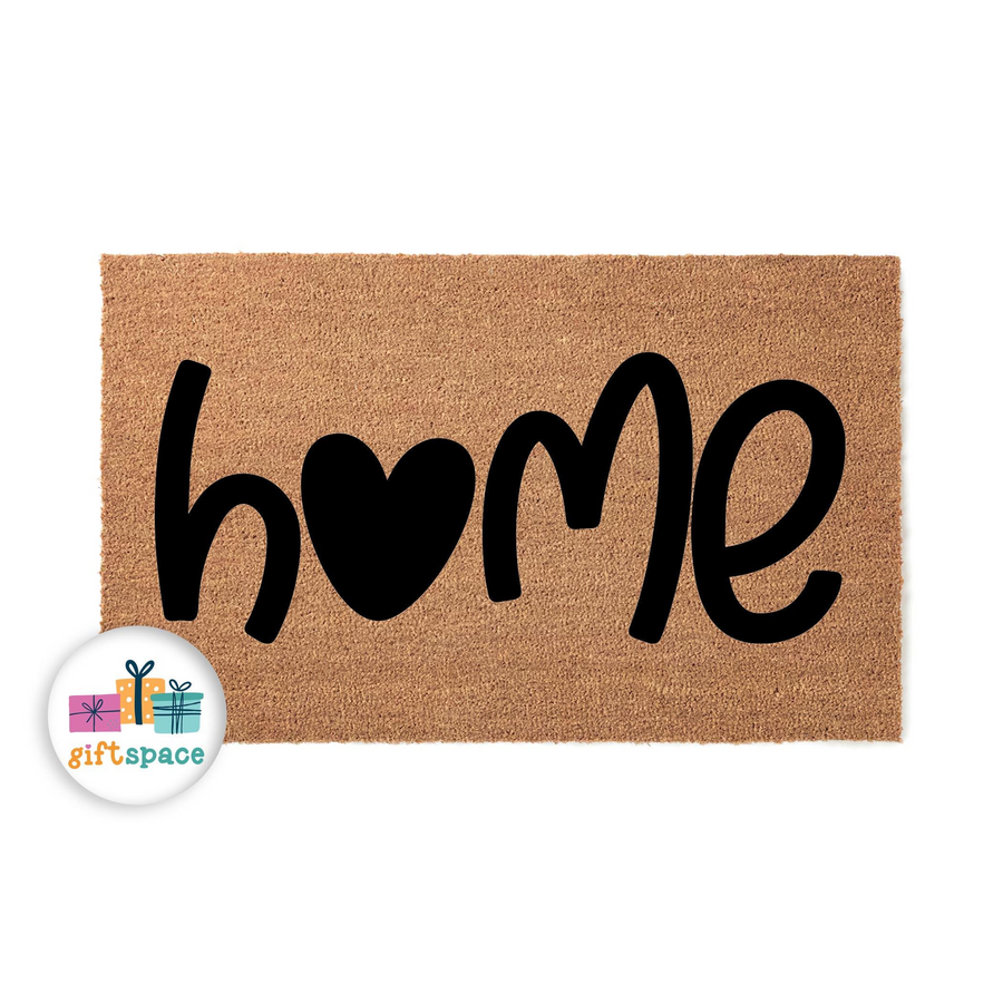 Home heart coir doormat featuring a natural brown fiber texture and bold black lettering where the letter o is replaced by a solid black heart shape, creating a welcoming entryway decor piece for a house or apartment front porch.
